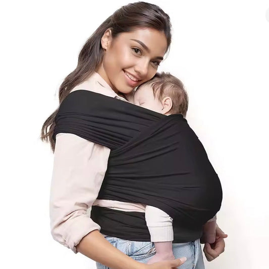 Woman holding a baby in a black wrap carrier against a white background